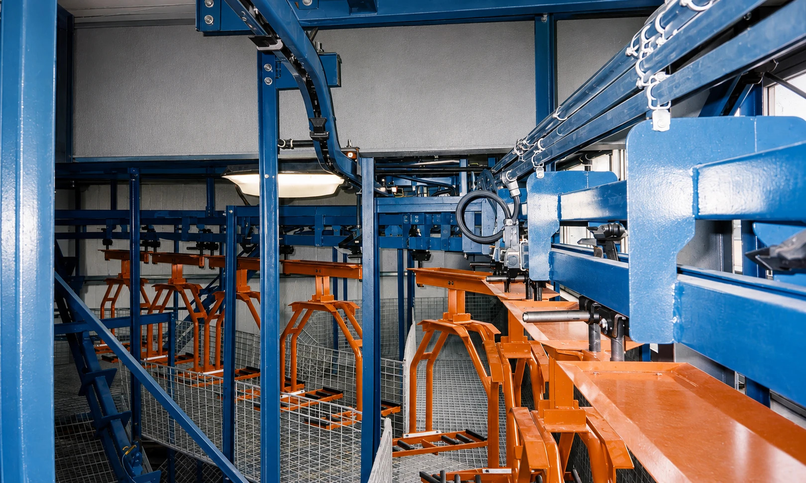 Close view of blue conveyor track, carrier mechanisms and orange suspended fixtures